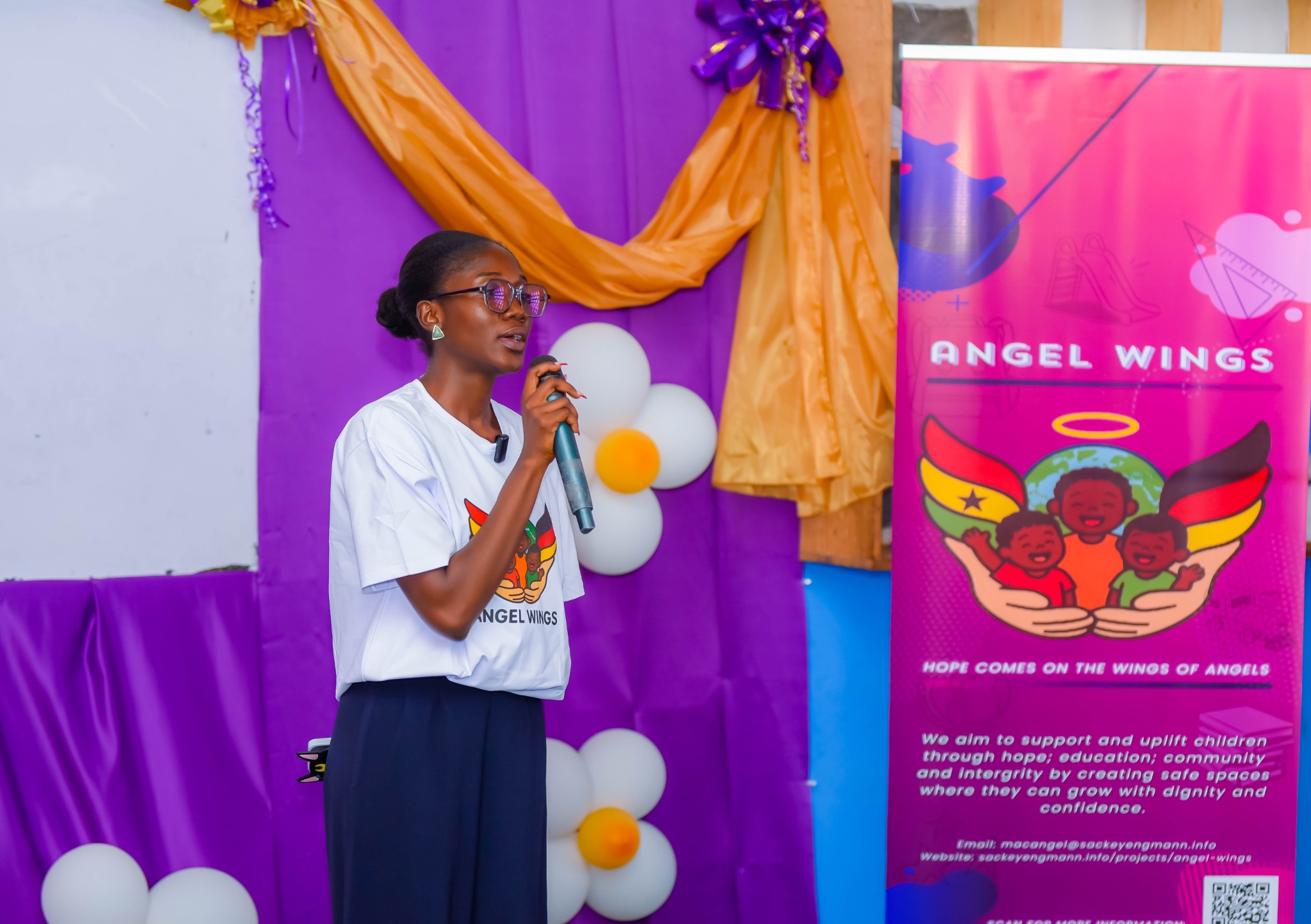 An Angel Wings volunteer speaking beside the project banner